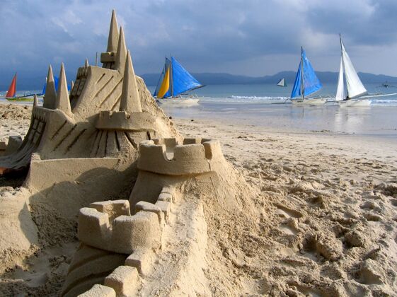 海洋近景拍摄沙滩上的沙堡 背景是小船户外小海洋