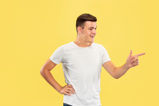 男性黄色工作室背景上的白人年轻人半身肖像穿着衬衫的漂亮男模人类情感的概念 面部表情 销售 广告指向侧面 看起来很开心事业帅气年轻