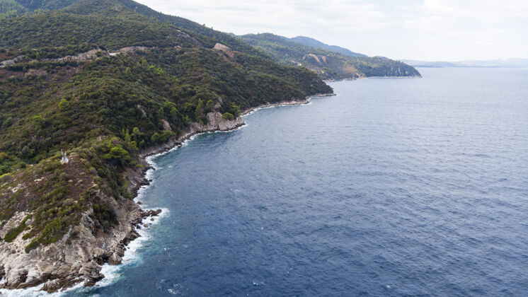 山爱琴海沿岸有蓝色透明的海水 周围绿树成荫 岩石 灌木丛和树木 从无人机希腊俯瞰海滩观点希腊