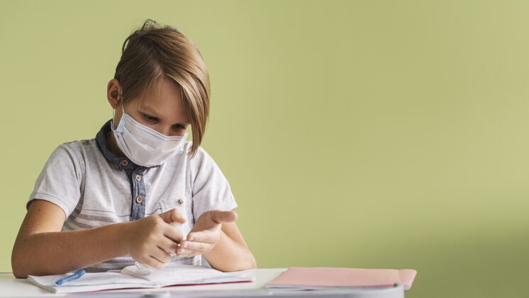 冠状病毒带医用面罩的儿童正面图 在课堂上消毒双手 有复印空间新常态病毒学校