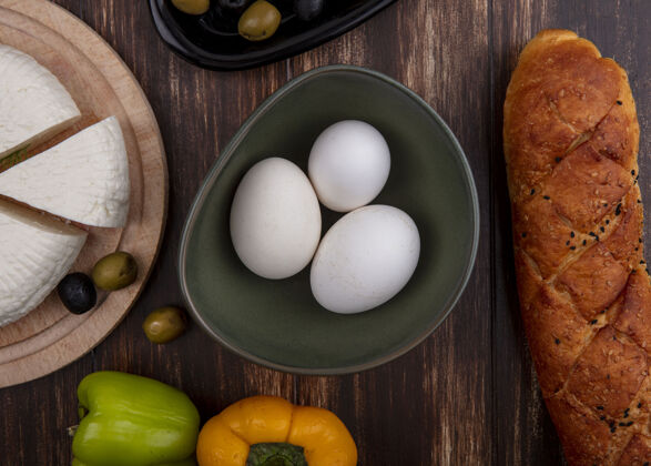 木头顶视图：鸡蛋放在碗里 芝士放在架子上 甜椒和面包放在木制背景上奶酪面包羊奶