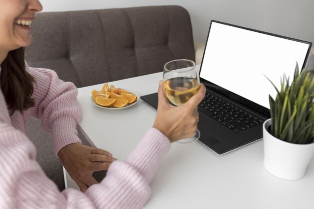 笔记本电脑笑脸女人在家和朋友一起用笔记本电脑和饮料庆祝病毒房子聚会