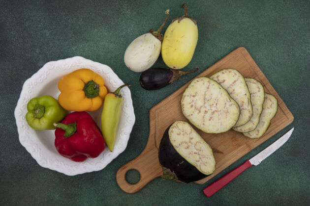 板子俯视图茄子片在一个切菜板上用刀与甜椒在一个盘子上的绿色背景切片盘子景
