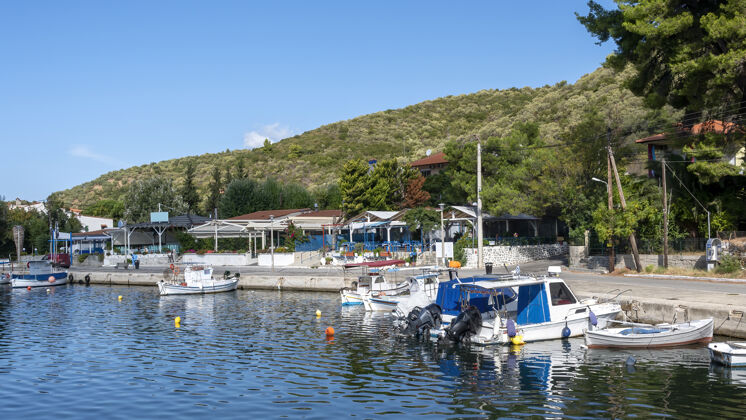 海停泊在河堤附近的船街上有建筑物和餐馆 绿树成荫 绿山成荫 希腊观点海景海洋