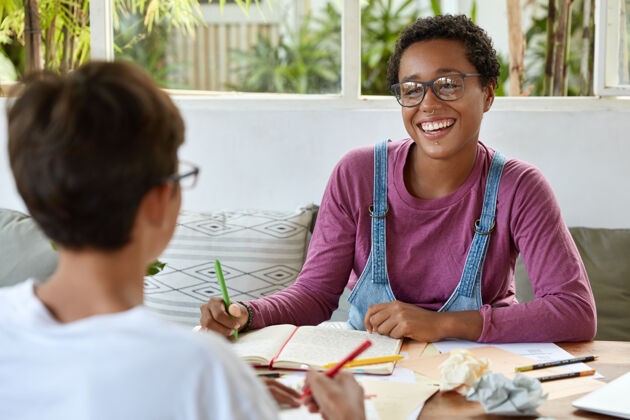 组织者年轻和同事的概念戴着眼镜 面带微笑的黑皮肤女士 戴着穿孔眼镜 和她的同事合作 做共同的任务 准备家庭作业 讨论教育问题采访合作日记
