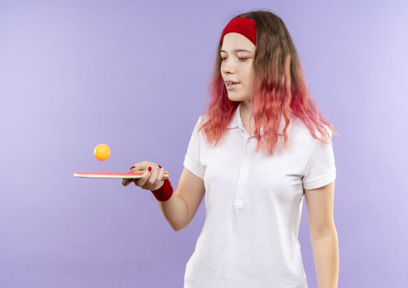 女人戴着头巾 拿着乒乓球拍和球 脸上带着微笑站在紫色墙壁上玩耍的年轻女子头带玩运动