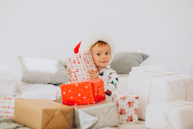 可爱戴圣诞帽的可爱男孩在圣诞节打开礼物礼物灯帽子
