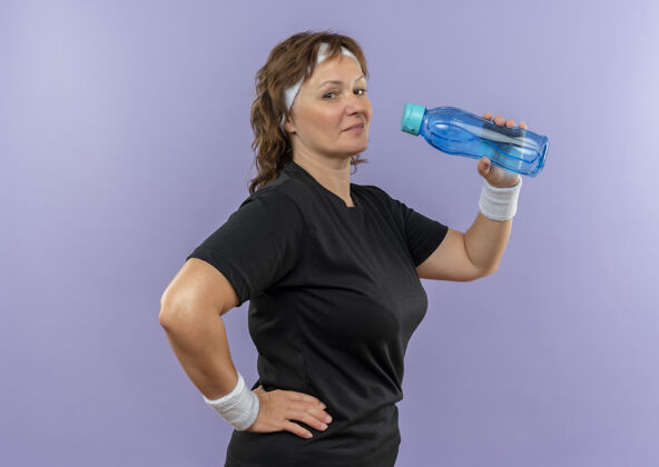 运动中年运动女性 身穿黑色t恤 戴着头巾 下班后站在蓝色的墙上喝水工作看后