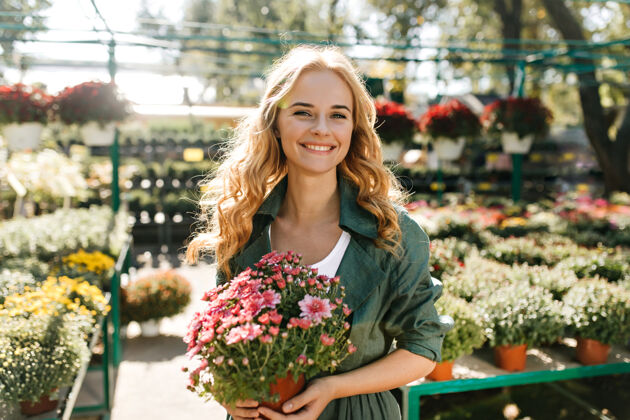 享受一位金发碧眼 笑容温柔的年轻女子 身着绿色长袍 系着腰带 正在温室里工作可爱公园植物