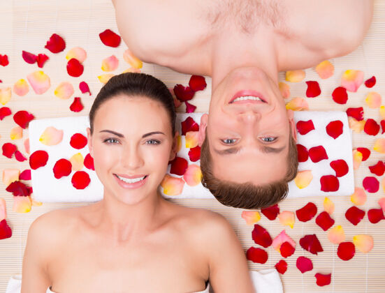 浪漫美丽的年轻夫妇躺在玫瑰花瓣里放松沙龙书桌面部