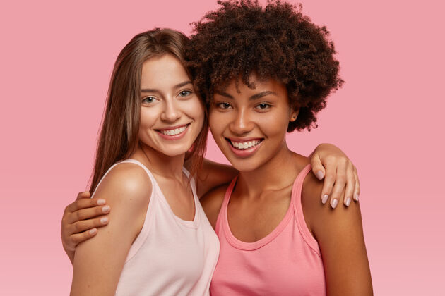 风格积极微笑 不同的好朋友互相拥抱 有友好的关系 合影留念 高兴相见 隔着粉色的墙跨种族的友谊 支持的理念肖像姿势牙齿