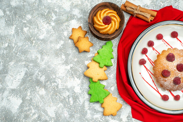 景观顶视图：白色椭圆形盘子上的浆果蛋糕 红色披肩 灰色表面上的奇纳蒙饼干 复制空间饼干生的盘子