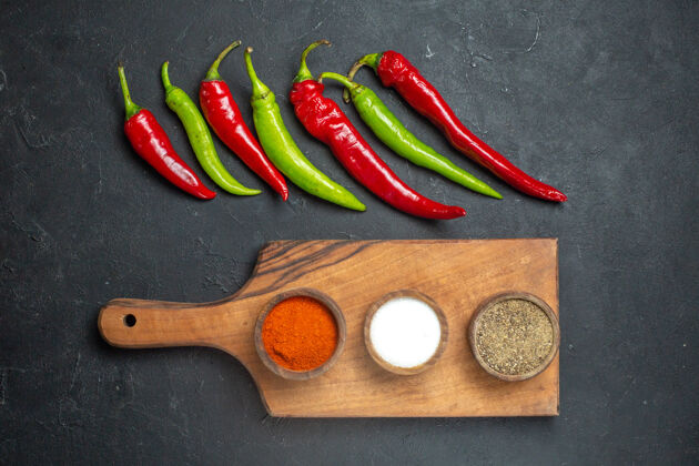 菜板顶视图横排青椒和红椒不同的香料放在砧板上深色的表面上划船蔬菜观点