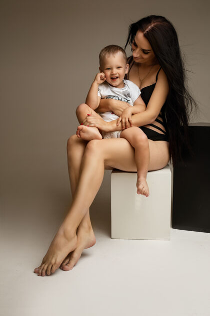 母性年轻可爱的妈妈穿着内衣赤裸着双腿拥抱着小男孩亲子关系裸体女人