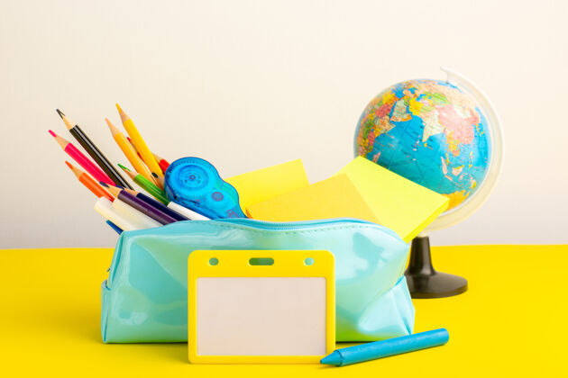 地球仪正面图不同颜色的铅笔在蓝色的笔盒里 黄色的桌子上有一个小地球仪记事本图形艺术盒子