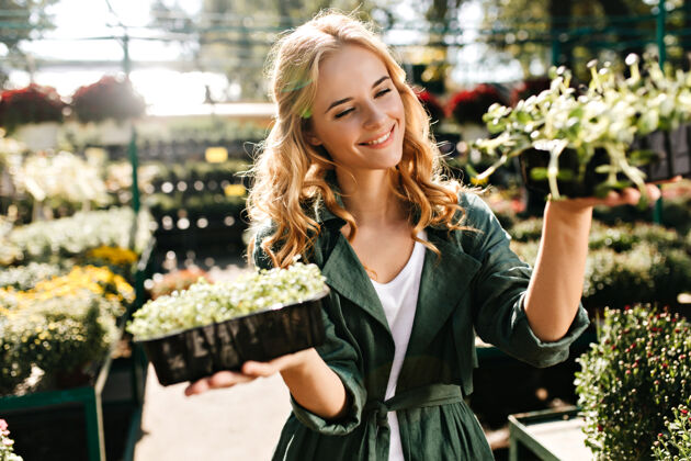 表情一位金发碧眼 笑容温柔的年轻女子 身着绿色长袍 系着腰带 正在温室里工作脸植物温室