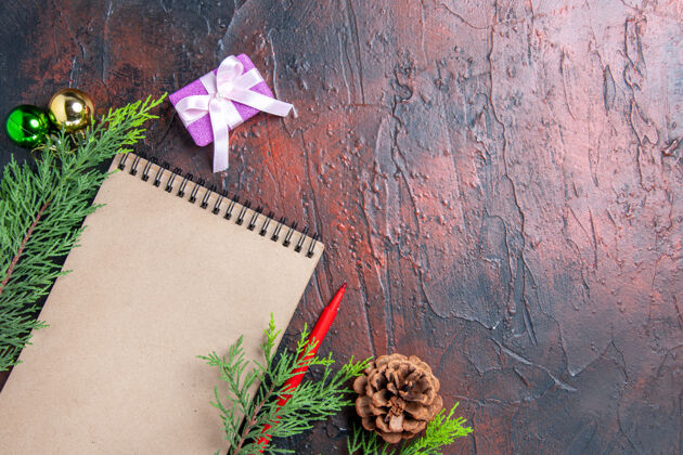 顶部顶视图红色钢笔笔记本松树枝圣诞树球玩具和礼物暗红色表面与自由空间圣诞视图钢笔