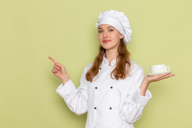 护士身着白色厨具套装的女厨师手持一杯咖啡 微笑着坐在绿色桌子上 厨房烹饪美食 女性色彩前面西装衣服