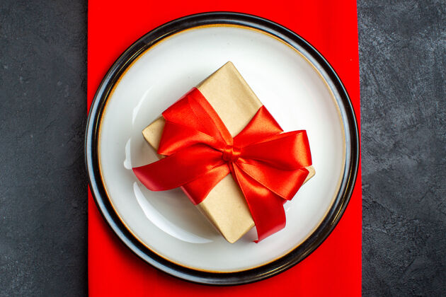 视图国家圣诞餐背景俯视图 黑色背景上的红色餐巾上的空盘子上有蝴蝶结形状的红丝带圣诞节弓餐巾