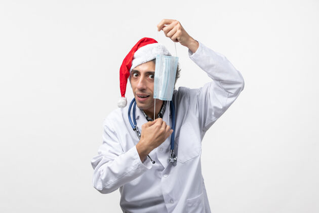 视图正面图男医生拿着口罩在白墙上共舞新年假期病毒球员制服病毒