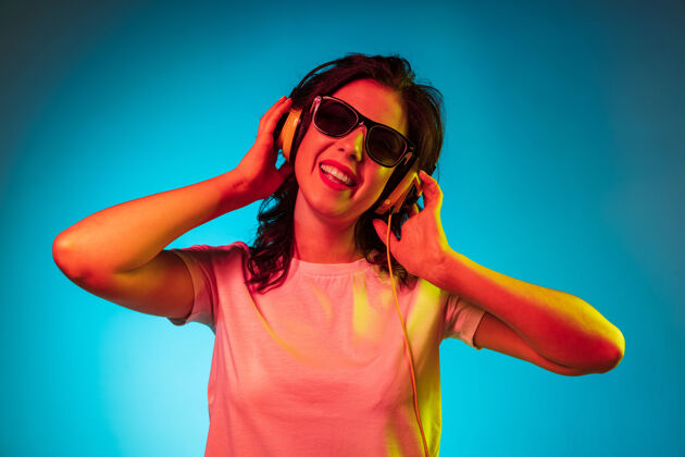 年轻快乐的年轻女子站在时尚的蓝色霓虹灯工作室 戴着墨镜微笑着派对迪斯科站