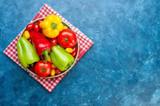 各种蔬菜顶视图各种蔬菜樱桃西红柿不同颜色甜椒西红柿孜然花放在盘子上红白格子厨房毛巾放在蓝色桌子上复制位置樱桃不同的各种