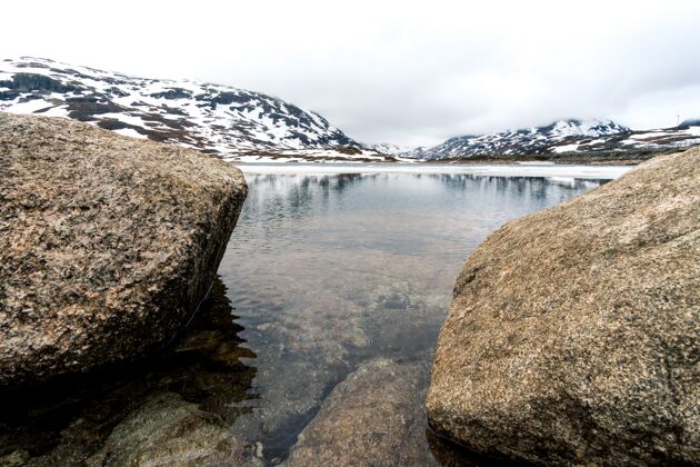 丘陵挪威河边和雪山上美丽的岩石照片挪威海云