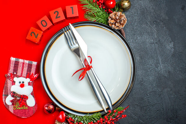 盘子餐盘上餐具的俯视图装饰配件杉木树枝和数字圣诞袜在黑色背景上的红色餐巾上鼓分支杉木