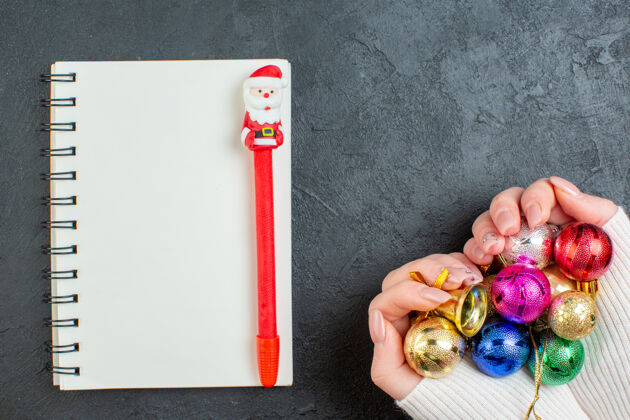 顶部手持彩色装饰配件笔记本顶视图 黑色背景上有钢笔视图圣诞节花
