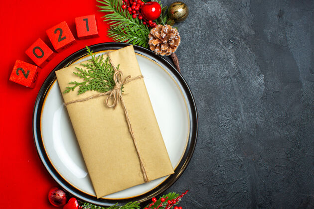 数字新年背景顶视图 餐盘上有礼物装饰配件杉木树枝和数字 在黑色桌子右侧的红色餐巾上右侧顶部壁板