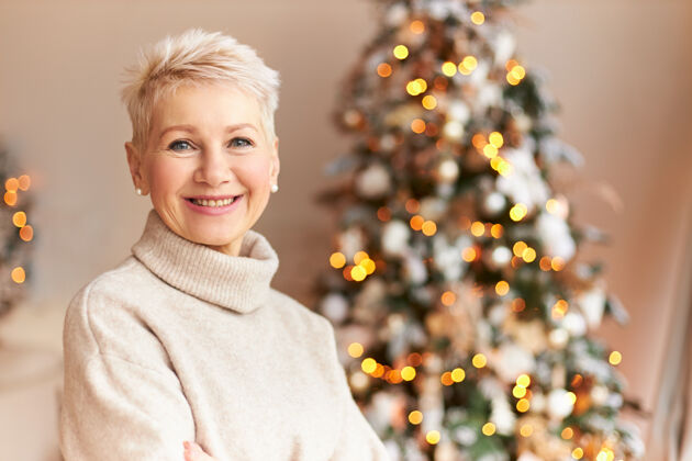 圣诞节季节 冬季 节日和庆祝概念图为快乐的中年女士 短发 灿烂的笑容 享受着圣诞节的准备 在家中装饰的松树前摆姿势节日室内季节