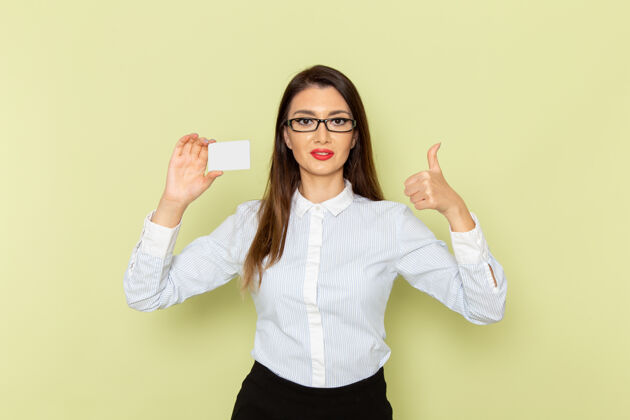浅绿色身穿白衬衫和黑裙子的女上班族手持浅绿色墙上的塑料卡的正面图塑料办公室女性