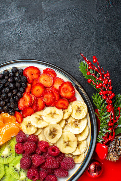 分支餐桌上收集新鲜水果的垂直视图装饰配件杉木树枝和数字在黑色背景上的红色餐巾上饮食新鲜冷杉