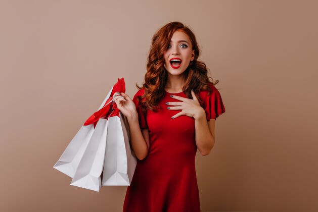 服装快乐的长发年轻女子在购物后摆姿势无忧无虑的姜女士拿着购物袋购物者微笑红发