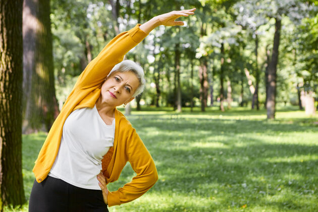伸展活力 健康 幸福和退休概念美丽的运动型老年女性 短发侧弯 手臂伸直退休女性在公园或森林户外锻炼休闲老年运动