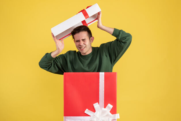 微笑前面的景象吓坏了一个年轻人 他站在黄色的大礼品盒后面 带着盒盖封面盒子成人