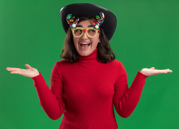 年轻穿着红毛衣的年轻女孩戴着滑稽的眼镜和黑帽子看着镜头开心而积极毛衣相机女孩