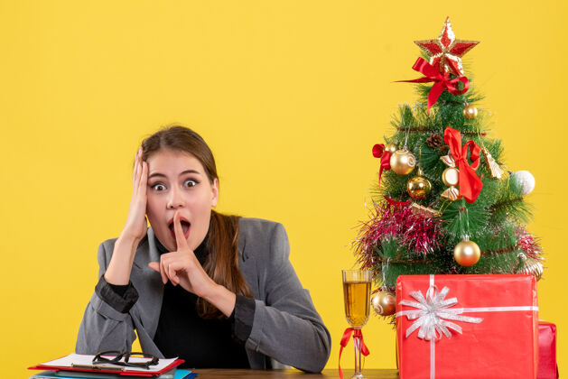 商人前视图惊讶的女孩坐在桌子旁做嘘标志圣诞树和礼物鸡尾酒桌子圣诞节标志