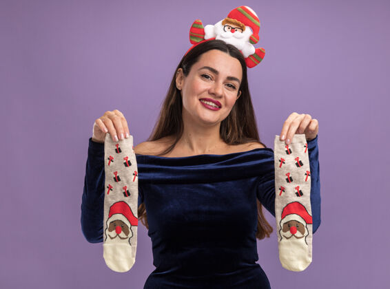 圣诞节微笑着的年轻漂亮的女孩穿着蓝色的裙子 戴着圣诞发箍 手里拿着圣诞袜 背景是紫色的年轻人衣服微笑
