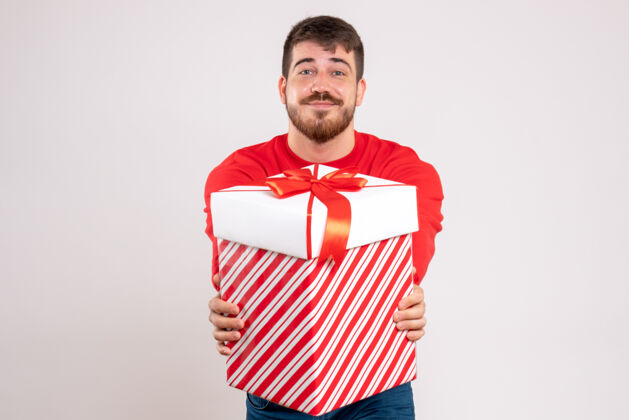 前面前视图中的年轻人在红衫举行圣诞礼物盒在白色的墙壁上人抱着快乐