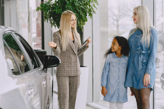 快乐一家人在汽车沙龙里买车的女人和妈妈在一起的非洲小女孩和客户在一起的经理汽车女人经销商