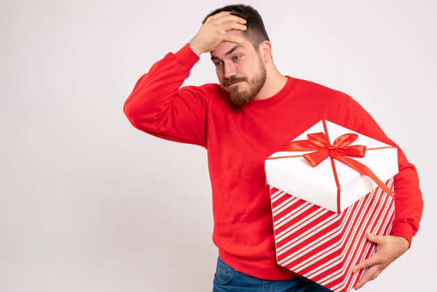 男性前视图中的年轻人在红衫举行圣诞礼物盒在白色的墙壁上圣诞节礼物年轻男性