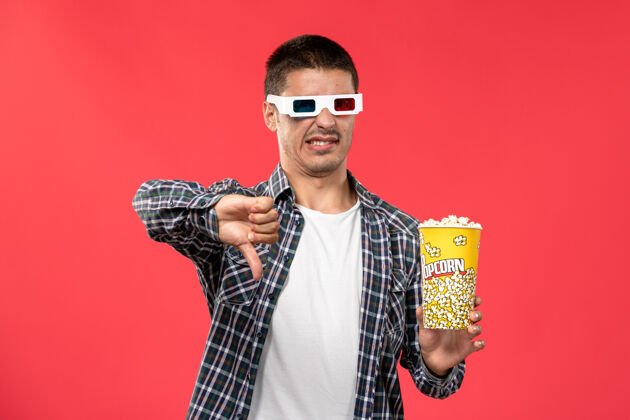 成人正面图年轻男子手持爆米花包在浅红墙电影院看电影男性浅红色电影院