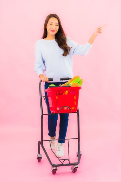 超市一幅美丽的亚洲年轻女子的画像 粉红色的隔离墙上 篮子里放着水果蔬菜和杂货市场水果新鲜