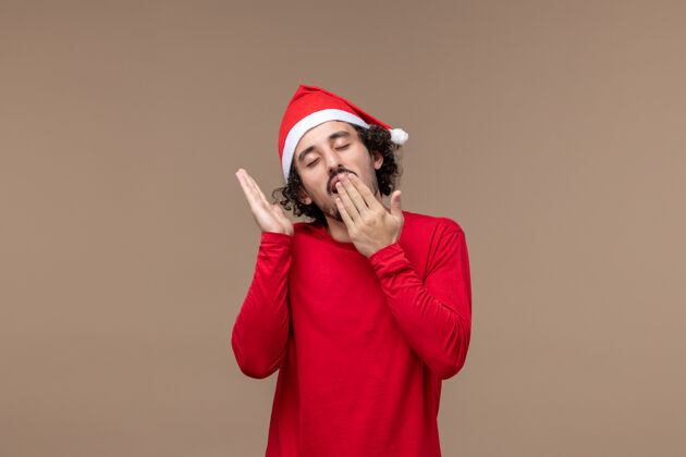 尝试正面图年轻男子打哈欠 试图在棕色背景上睡觉圣诞节情绪圣诞节睡眠歌手