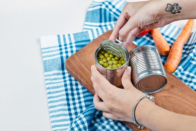 有机手拿一罐煮青豌豆放在一张白色的桌子上 桌子上放着蔬菜和桌布大理石小吃烹饪