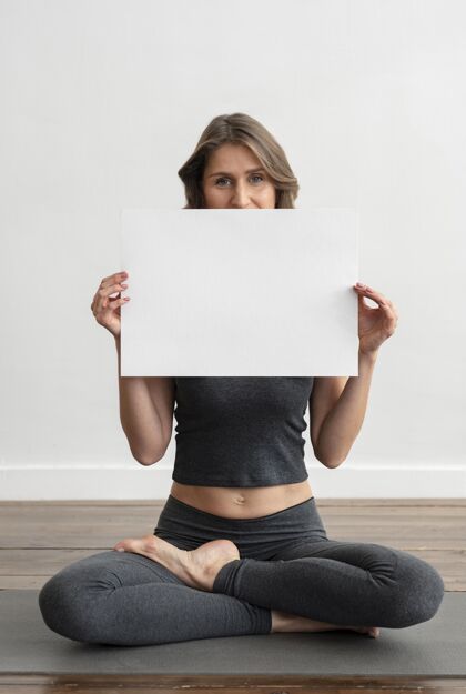 瑜伽前视图的妇女持有空白标语牌 而做瑜伽休闲垫子反省