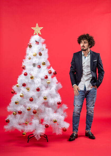 快乐圣诞庆典上 留着胡子的年轻人站在圣诞树旁看着什么东西装饰庆祝东西