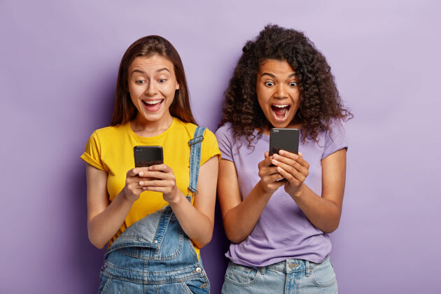 种族照片中快乐的女性朋友们无视现场交流 通过手机在博客上聊天 用积极的表情凝视屏幕高兴打字购物