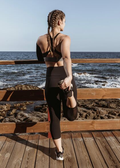 工作在海滩边伸展运动的女人的后视图户外体育锻炼体育